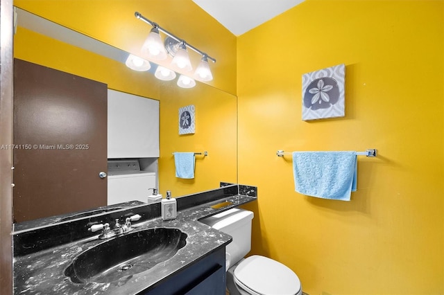 bathroom featuring vanity, washer / dryer, and toilet