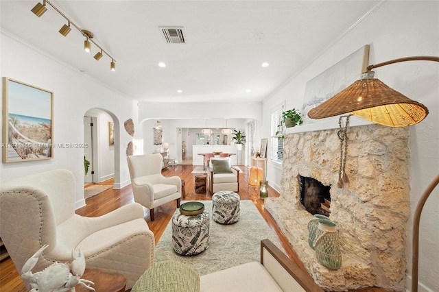 living room featuring wood-type flooring, a stone fireplace, track lighting, and crown molding