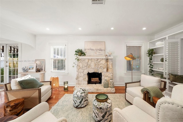 living room featuring crown molding, a fireplace, light hardwood / wood-style flooring, and french doors