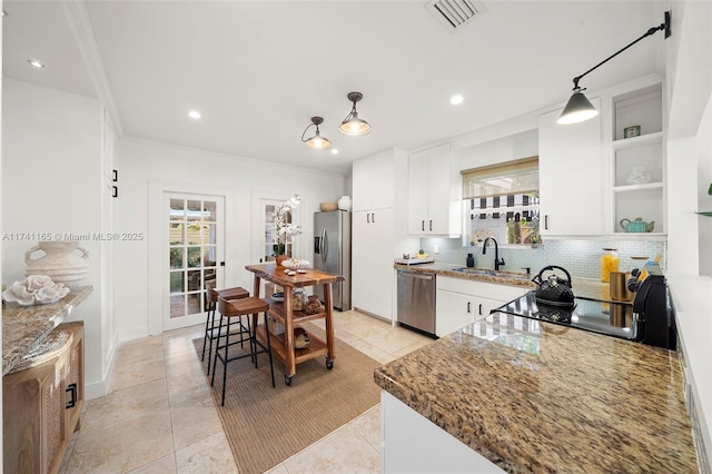 kitchen featuring stainless steel appliances, white cabinets, dark stone counters, and decorative light fixtures