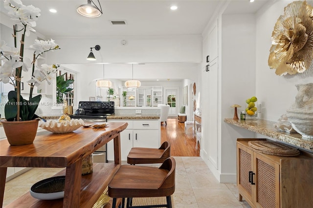 kitchen with decorative light fixtures, white cabinets, decorative backsplash, kitchen peninsula, and light stone countertops