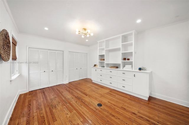 unfurnished bedroom with crown molding, hardwood / wood-style flooring, a chandelier, and two closets