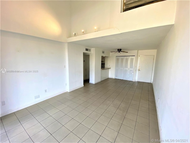 tiled empty room with ceiling fan and a towering ceiling