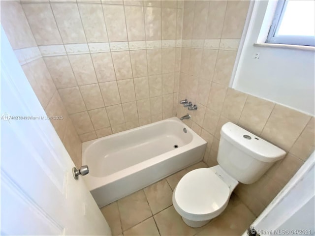 bathroom with bathing tub / shower combination, tile walls, tile patterned floors, and toilet