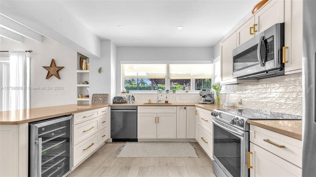 kitchen featuring sink, appliances with stainless steel finishes, white cabinetry, kitchen peninsula, and beverage cooler