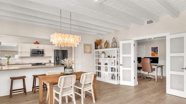 dining area featuring beam ceiling, light hardwood / wood-style floors, french doors, and a chandelier