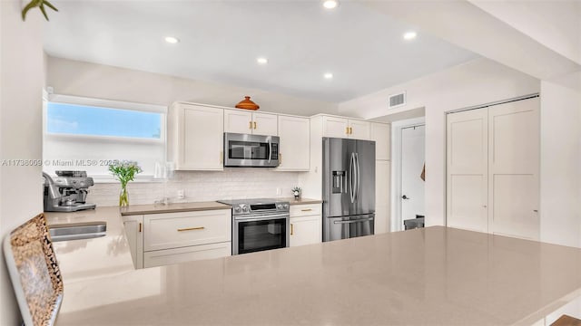 kitchen featuring appliances with stainless steel finishes, white cabinetry, sink, backsplash, and kitchen peninsula