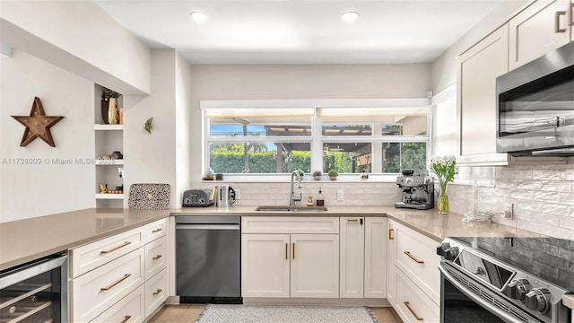 kitchen with sink, appliances with stainless steel finishes, wine cooler, white cabinets, and kitchen peninsula