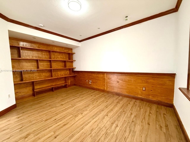 unfurnished room featuring light wood finished floors, ornamental molding, wood walls, and wainscoting