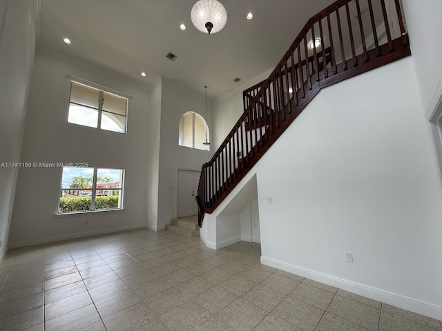 unfurnished living room with baseboards, a high ceiling, visible vents, and stairs