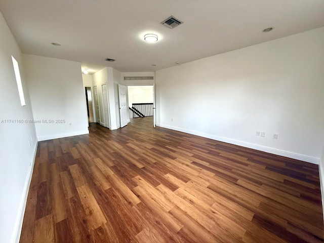 empty room with baseboards, visible vents, and dark wood finished floors