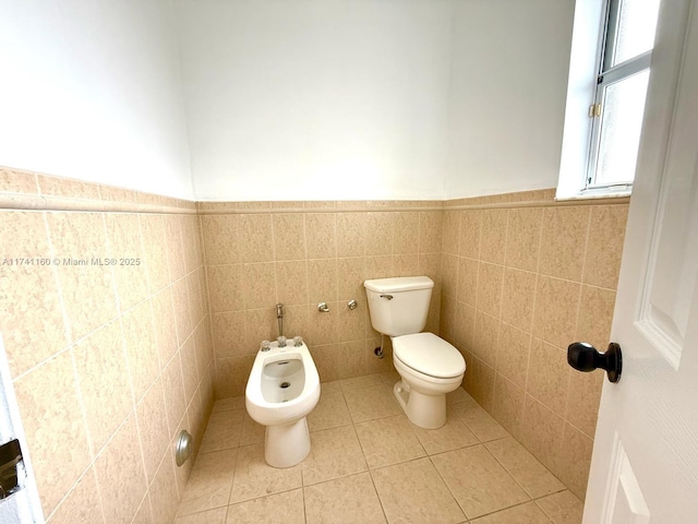 half bath featuring tile patterned flooring, toilet, tile walls, wainscoting, and a bidet