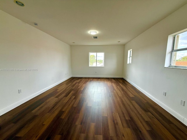 spare room featuring visible vents, baseboards, and dark wood-type flooring