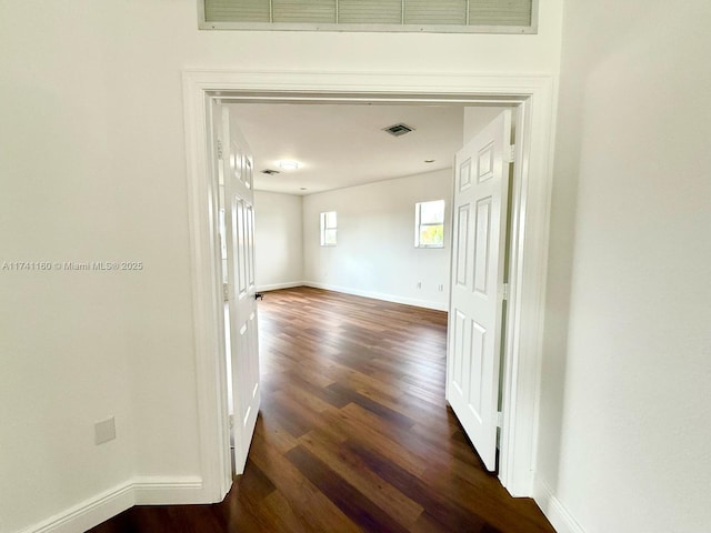 hall with dark wood-type flooring, visible vents, and baseboards