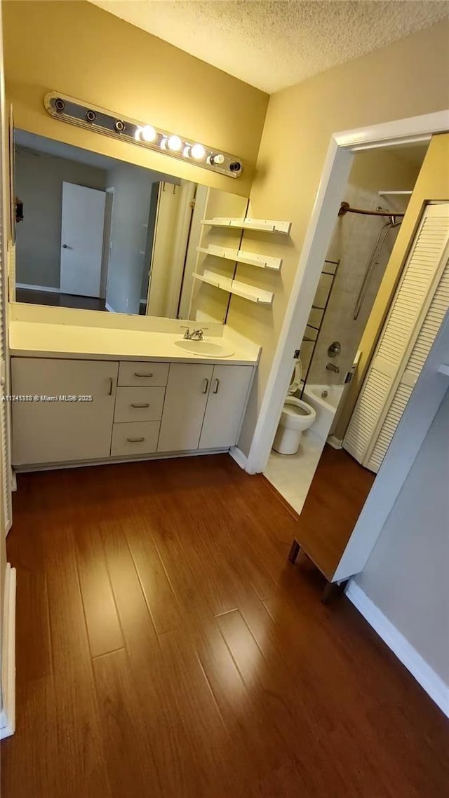 full bathroom featuring wood-type flooring, vanity, toilet, a textured ceiling, and washtub / shower combination