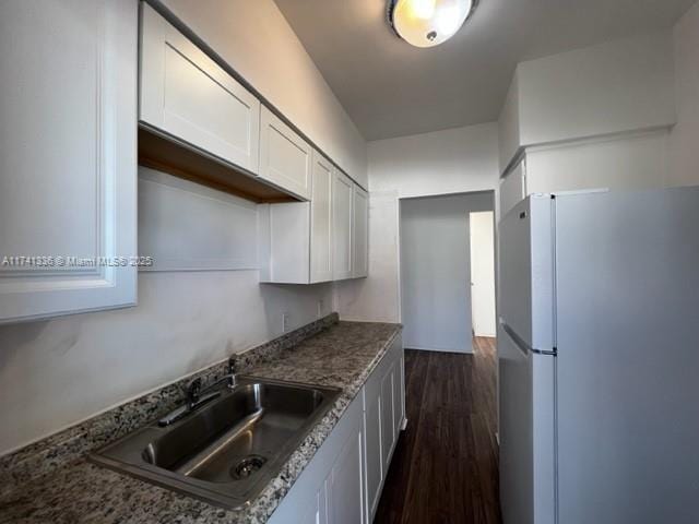 kitchen featuring sink, dark stone countertops, dark hardwood / wood-style floors, white refrigerator, and white cabinets