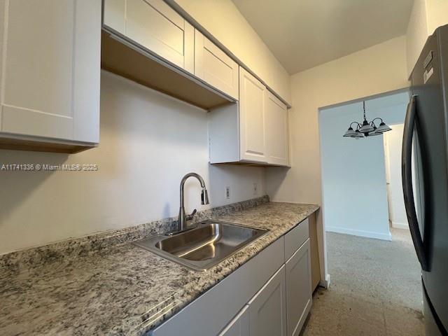 kitchen featuring black refrigerator, sink, white cabinets, and an inviting chandelier