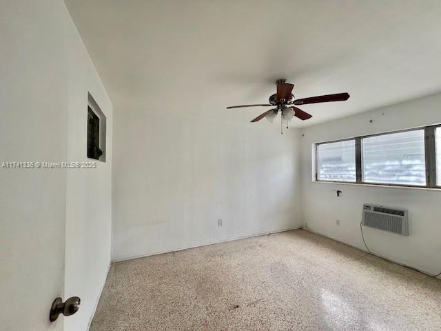 unfurnished room with ceiling fan and a wall unit AC