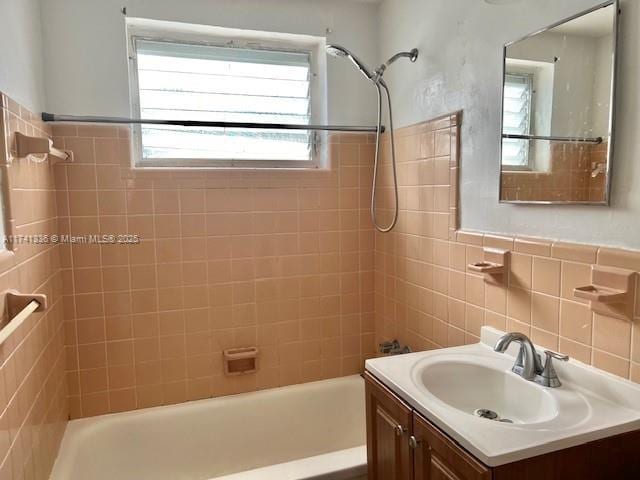 bathroom with vanity, tiled shower / bath combo, and tile walls