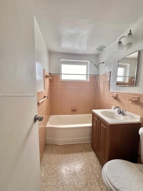 full bathroom with tile walls, vanity, toilet, and tiled shower / bath