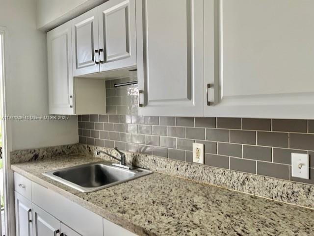 kitchen featuring white cabinetry, light stone counters, sink, and tasteful backsplash