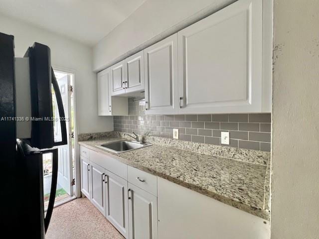 kitchen featuring sink, tasteful backsplash, light stone counters, black refrigerator, and white cabinets