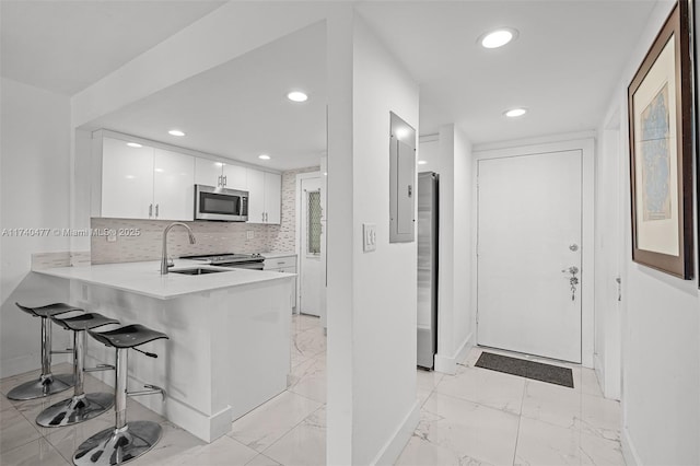 kitchen featuring appliances with stainless steel finishes, white cabinets, a kitchen bar, decorative backsplash, and kitchen peninsula