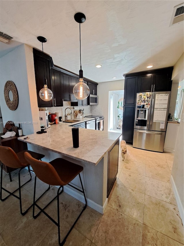 kitchen featuring dark cabinets, a peninsula, stainless steel appliances, visible vents, and pendant lighting