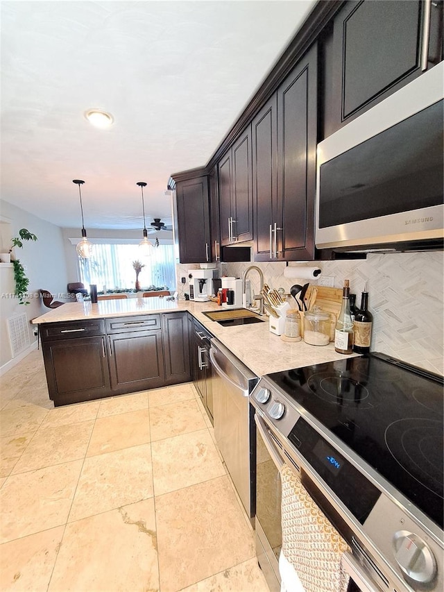 kitchen with stainless steel appliances, a peninsula, a sink, light countertops, and pendant lighting