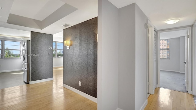 hallway featuring a tray ceiling and light hardwood / wood-style floors