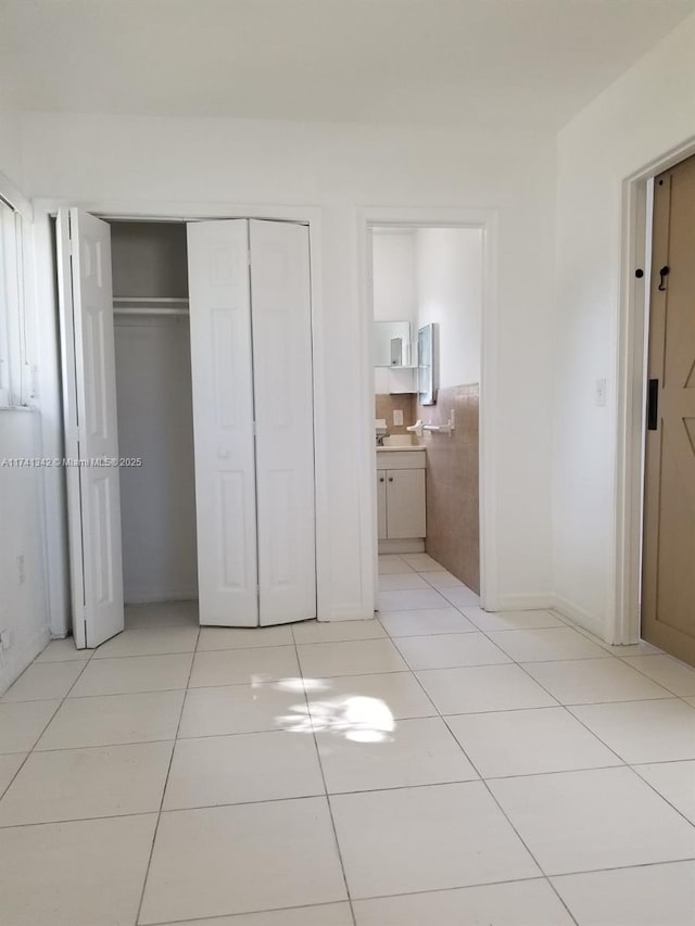 unfurnished bedroom featuring tile walls, connected bathroom, a closet, and light tile patterned flooring