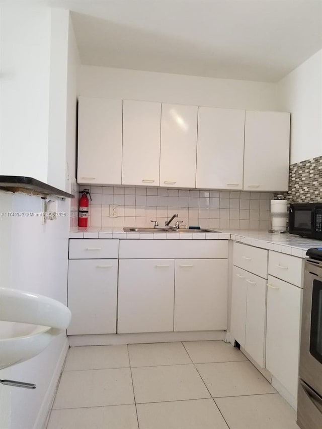 kitchen with sink, light tile patterned floors, stainless steel electric range, tasteful backsplash, and white cabinets