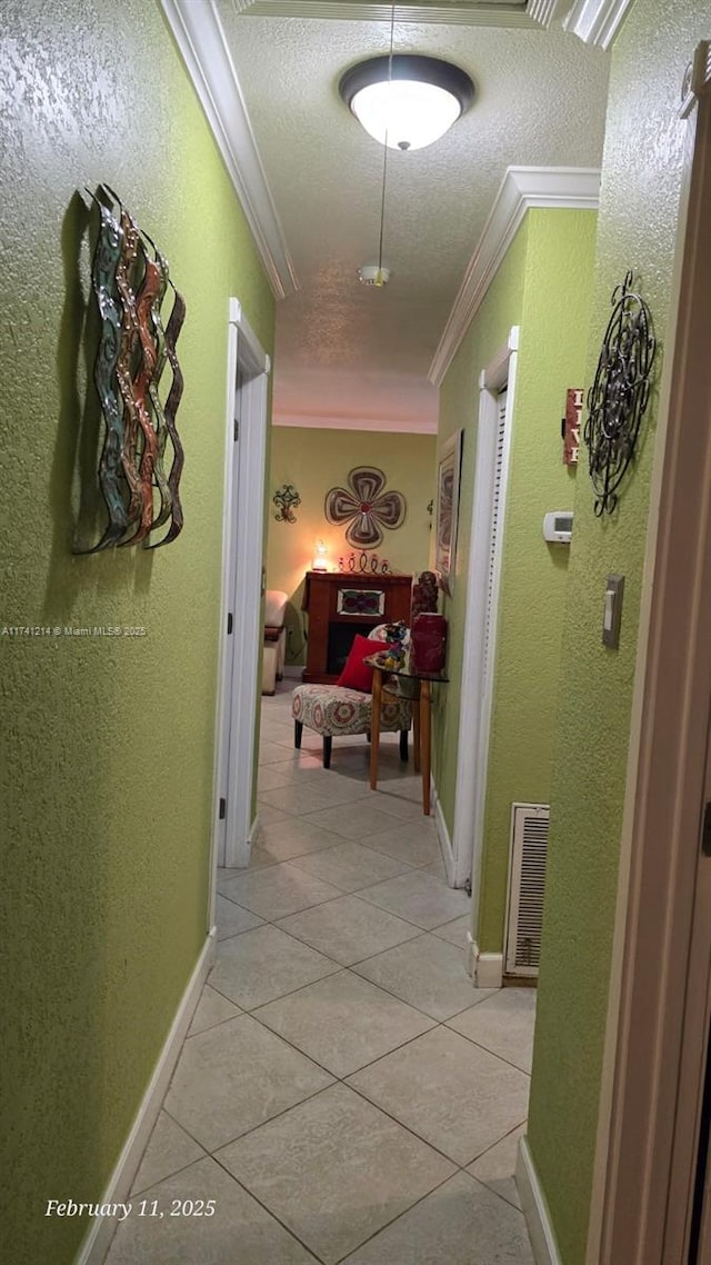 corridor featuring ornamental molding, a textured ceiling, and light tile patterned floors