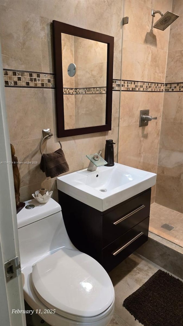 bathroom with vanity, tiled shower, tile walls, and toilet