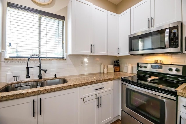 kitchen featuring sink, appliances with stainless steel finishes, white cabinetry, backsplash, and light stone counters