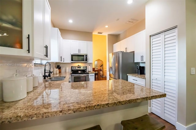 kitchen featuring appliances with stainless steel finishes, white cabinetry, sink, kitchen peninsula, and light stone countertops