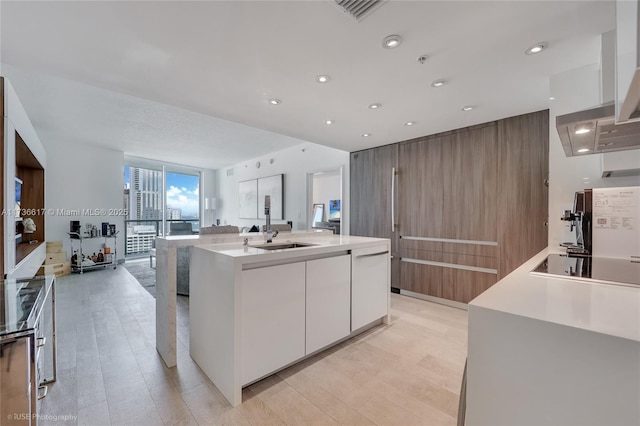 kitchen featuring sink, expansive windows, an island with sink, white cabinets, and black electric cooktop