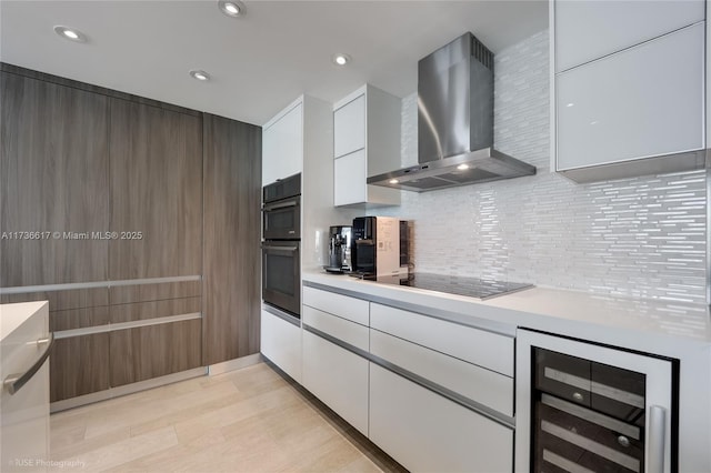 kitchen featuring wall chimney exhaust hood, white cabinets, beverage cooler, decorative backsplash, and black appliances