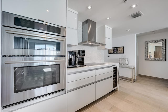 1900 N Bayshore Dr Unit 2004, Miami, FL 33132 - kitchen with wall chimney range hood, stainless steel double oven, white cabinetry, light wood-style flooring, and recessed lighting