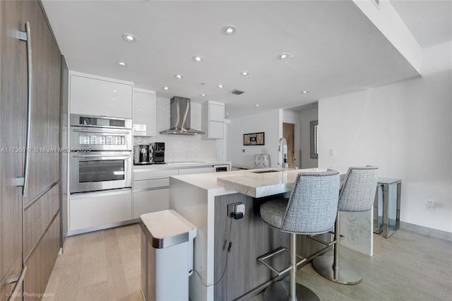 kitchen featuring sink, wall chimney exhaust hood, white cabinets, a kitchen island, and stainless steel double oven