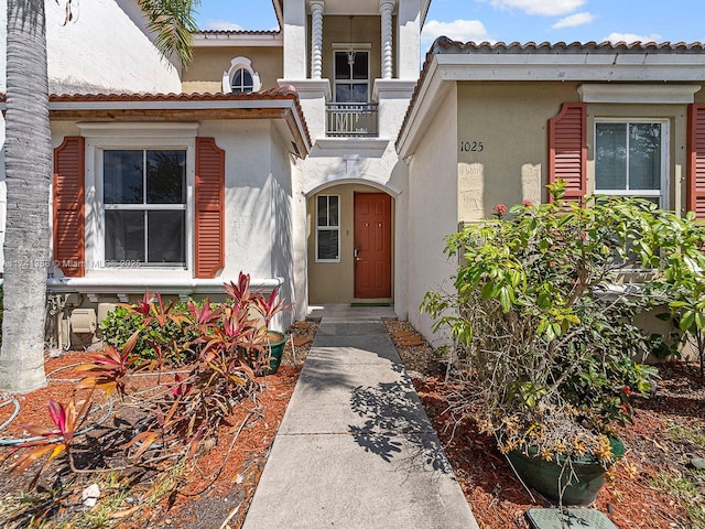 view of exterior entry with a tiled roof, a balcony, and stucco siding