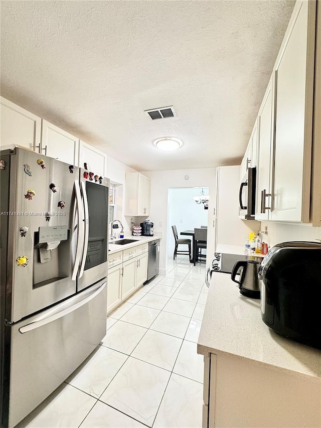 kitchen with sink, stainless steel appliances, a textured ceiling, white cabinets, and light tile patterned flooring