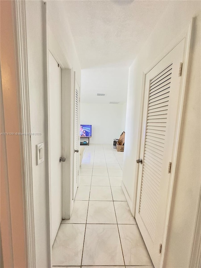 hallway with a textured ceiling and light tile patterned flooring