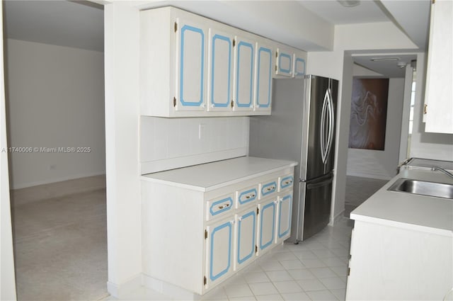 kitchen with blue cabinets, sink, light tile patterned floors, and stainless steel fridge