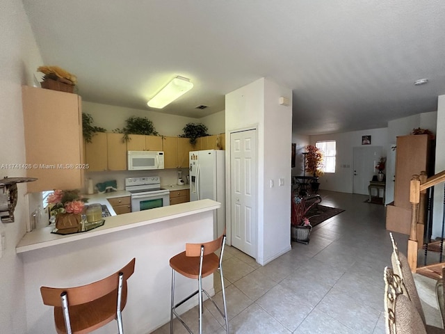 kitchen featuring light tile patterned flooring, a kitchen breakfast bar, kitchen peninsula, cream cabinets, and white appliances