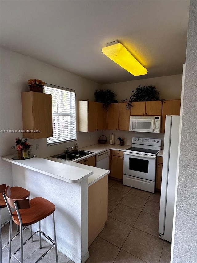 kitchen featuring light tile patterned flooring, sink, a kitchen breakfast bar, kitchen peninsula, and white appliances