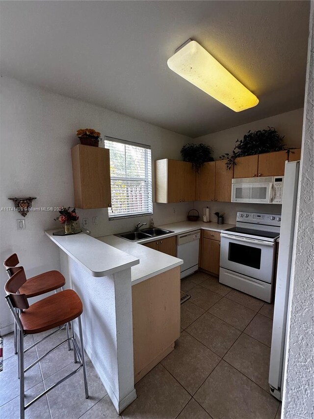 kitchen featuring a kitchen bar, sink, light tile patterned floors, kitchen peninsula, and white appliances