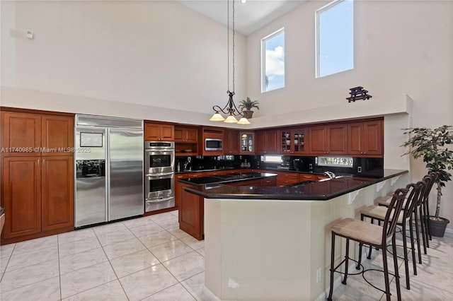 kitchen with sink, a breakfast bar area, built in appliances, hanging light fixtures, and kitchen peninsula