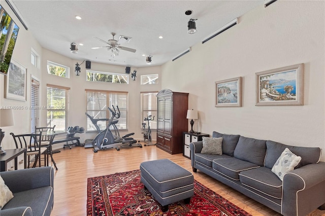 living room with ceiling fan, a towering ceiling, and light hardwood / wood-style floors