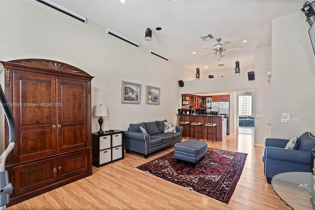 living room with a high ceiling, ceiling fan, and light wood-type flooring